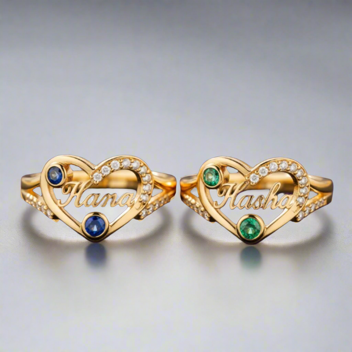 Two gold heart-shaped rings with gemstones on a gray background