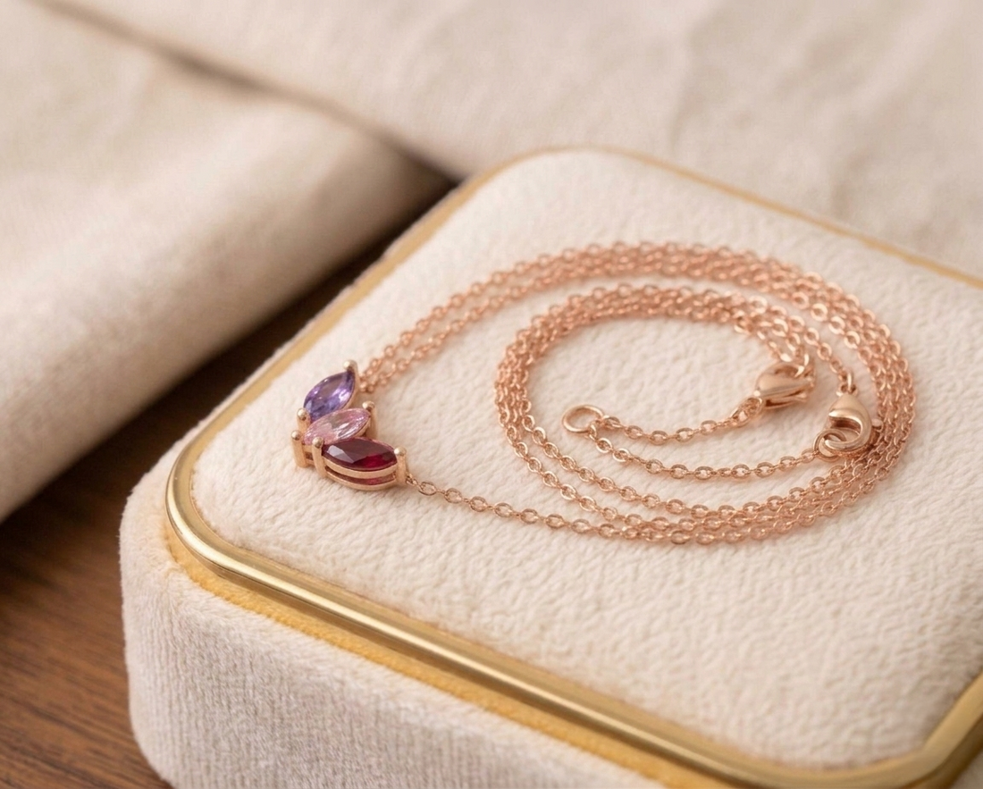 A personalized sterling silver family birthstone necklace with three round-cut stones (Amethyst, Emerald, and Ruby) on a dainty silver cable chain.