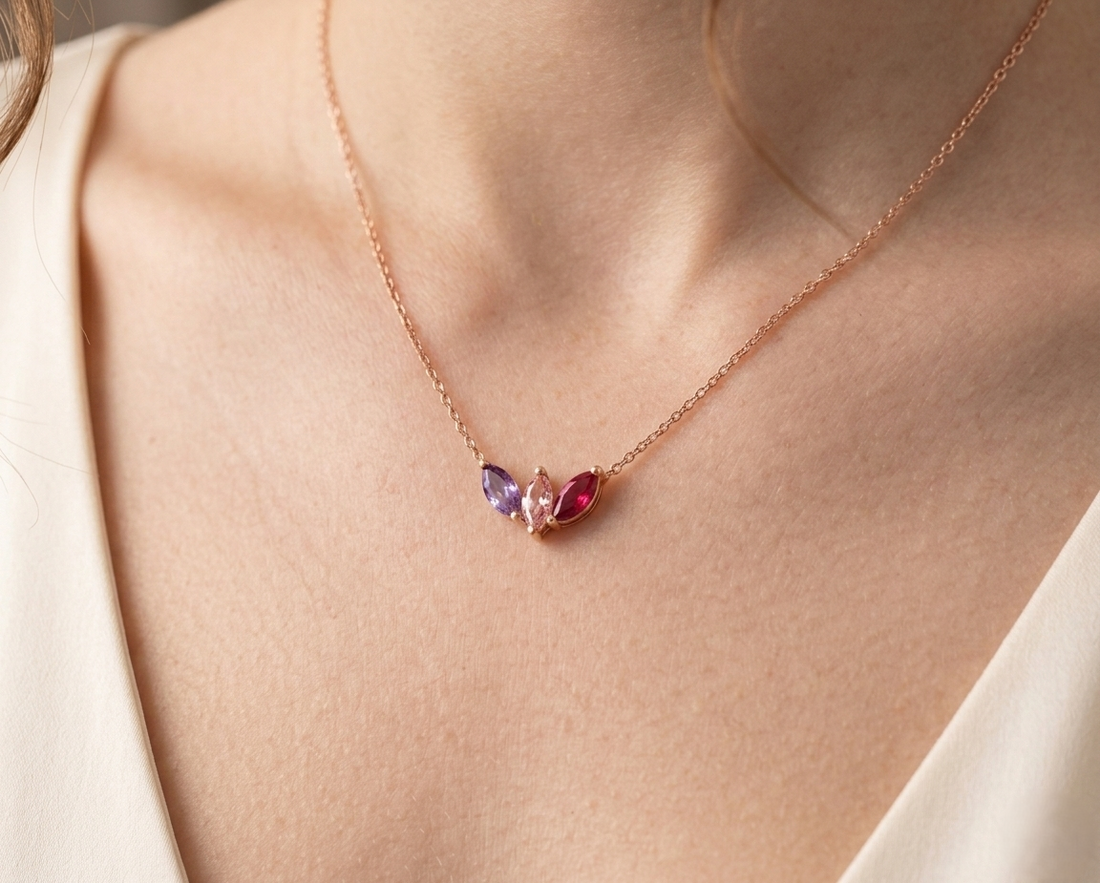 A personalized sterling silver family birthstone necklace with three round-cut stones (Amethyst, Emerald, and Ruby) on a dainty silver cable chain.