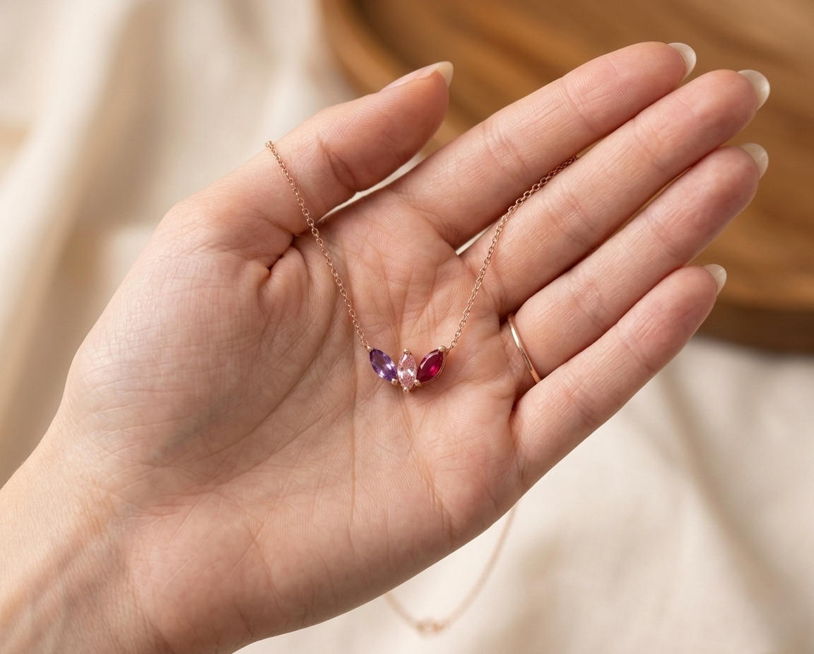 A personalized sterling silver family birthstone necklace with three round-cut stones (Amethyst, Emerald, and Ruby) on a dainty silver cable chain.