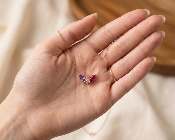 A personalized sterling silver family birthstone necklace with three round-cut stones (Amethyst, Emerald, and Ruby) on a dainty silver cable chain.